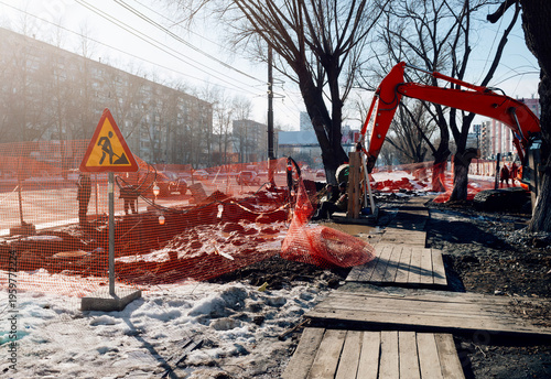 Excavator on the road. Road works on the street at spring city during the sunny day. Urban sidewalk construction with excavator