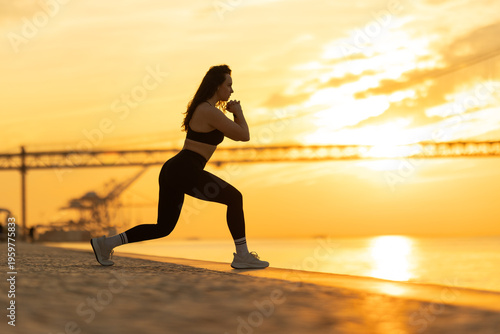 Woman exercising lunge on waterfront at sunset