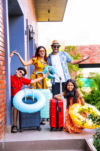 Young Indian parents and kids cheering on a porch with luggage for a vacation