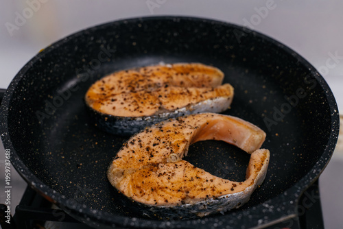 Fotografía Two fresh salmon steaks seasoned with black pepper and spices frying in a non-stick pan