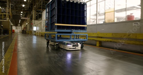 Autonomous mobile robot transporting a heavy blue cargo rack through a large industrial warehouse facility
