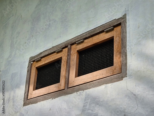 Two small wooden windows with mesh screens set in a textured gray plaster wall exterior
