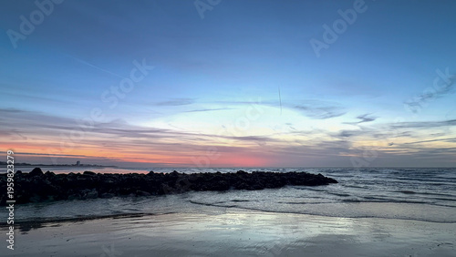 Peaceful sunset beach scene with rocky jetty and gentle waves at Nieuwpoort, Belgium
