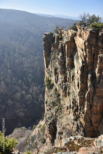 High vertical rock formations with a pronounced layered structure of a reddish-brown hue The deep gorge of the Maiden Rocks is a natural landmark of Bulgaria