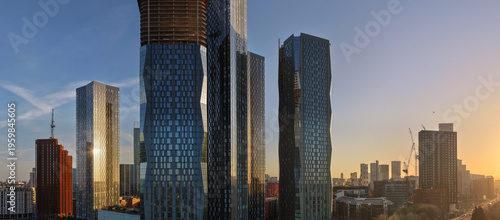Wide aerial panorama showing the dense skyscraper district of New Jackson with glassed facade towers during a golden sunrise in Manchester. 