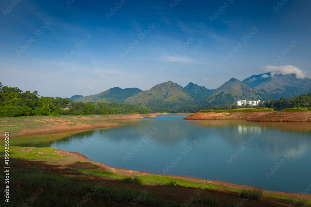 Obraz premium Scenic reflection of green peaks in a tropical reservoir under bright sunlight.