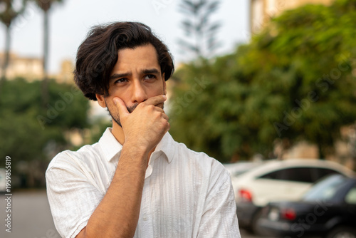 Portrait of a latin american man with a contemplative expression outdoors in front of a residential neighborhood.