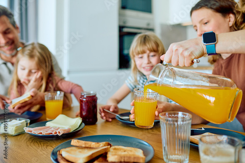 Foto Family enjoying morning breakfast, mother pouring orange juice for her daughter