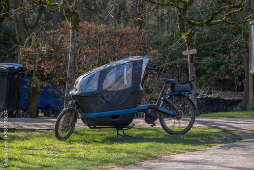 Electric cargo bike with child canopy parked in park, urban eco transport
