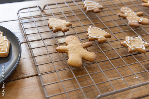 Gingerbread person cooling on wire rack at wooden tabletop with white icing and dark ceramic plate