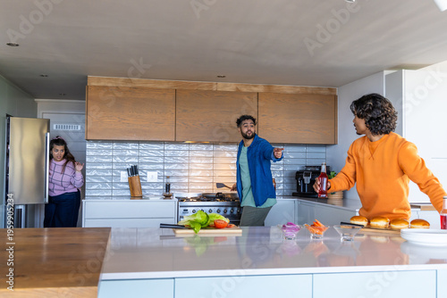 Diverse family with teen preparing burgers in kitchen using open fridge, buns and ketchup