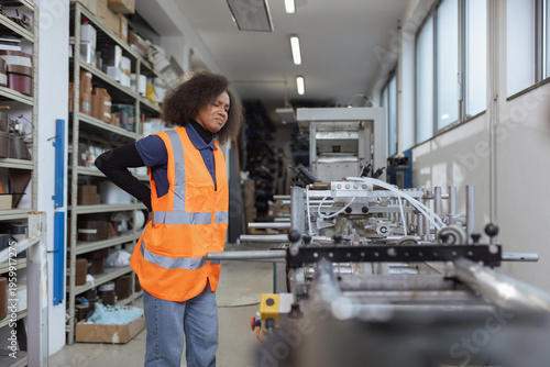 African American female industrial worker having physical workload and back pain while checking machinery, workplace injury in manufacturing