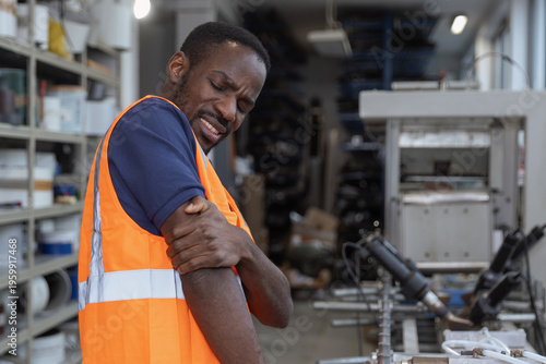 Worker in an orange safety vest experiencing upper arm pain, strain, fatigue, or injury caused by physical labor in workplace settings.