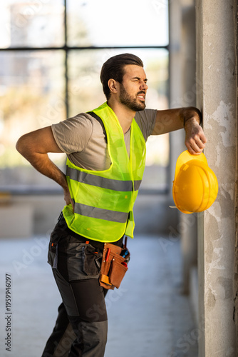 Construction worker feels back pain while resting with helmet on wall at building site during daytime