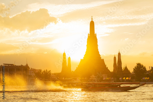 Wat arun temple silhouetted with long-tail boat creating splashes on chao phraya river at sunset