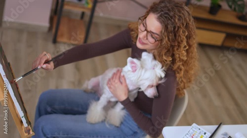 Woman painting on canvas while holding her dog