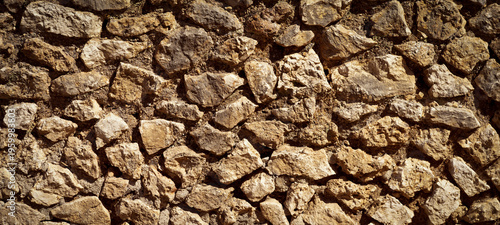 A fragment of an old wall made of stacked stones. A nateral background with a rough texture