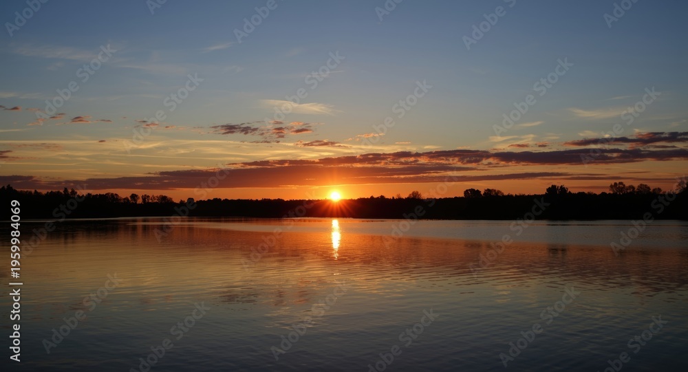 Fototapeta premium Golden sunset reflecting over calm water under a blue sky