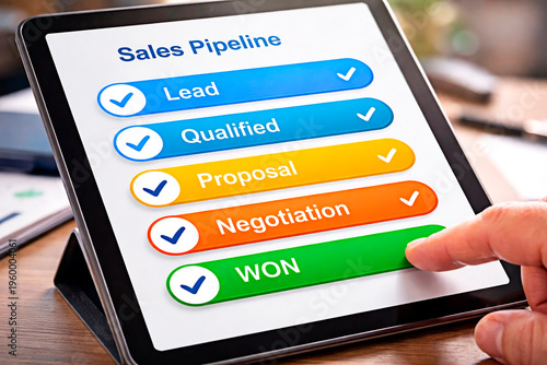 A person interacting with a tablet displaying a sales pipeline on a wooden desk in a modern office