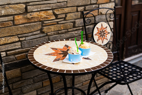 Two paper cups filled with delicious ice cream scoops sitting on a table at an outdoor summer cafe. Refreshing street food concept with blurred background and copy space
