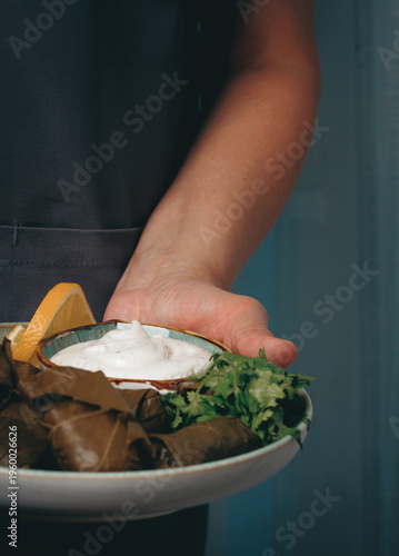 Schilderij op canvas A man holds a plate in his hands, a dolma with sauce and lemon.