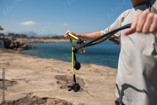 Obraz na płótnie Close-up of a man's hands holding a scuba diving regulator and yellow hose against a coastal background