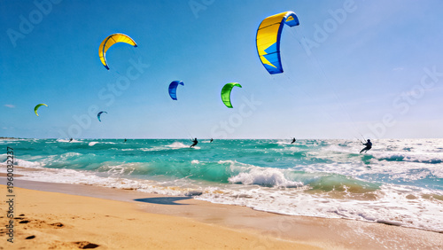 Group of kitesurfers riding waves in sea or ocean with colorful kites against blue sky. Sandy beach in foreground. Summer extreme sport, active lifestyle concept