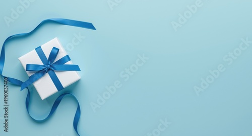 Flat lay of blue ribbon tied white gift on light blue surface with copy space for festive card