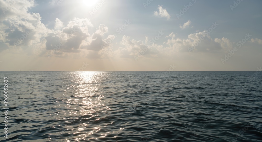 Obraz premium Mild sea surface shining under sunlight with calm ripples and a peaceful cloudy sky
