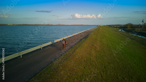 Aerial view of a lone bicycle tourist with panniers riding on Danube bike path near Bratislava, Slovakia. Bikepacking along river dike at sunset.