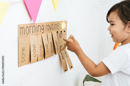 Little girl checking morning routine chart at home - Kid using DIY chore schedule - Learning and child development concept