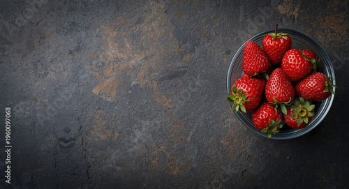 Red strawberries inside transparent bowl on dark textured concrete surface with rustic charm and wide copy space