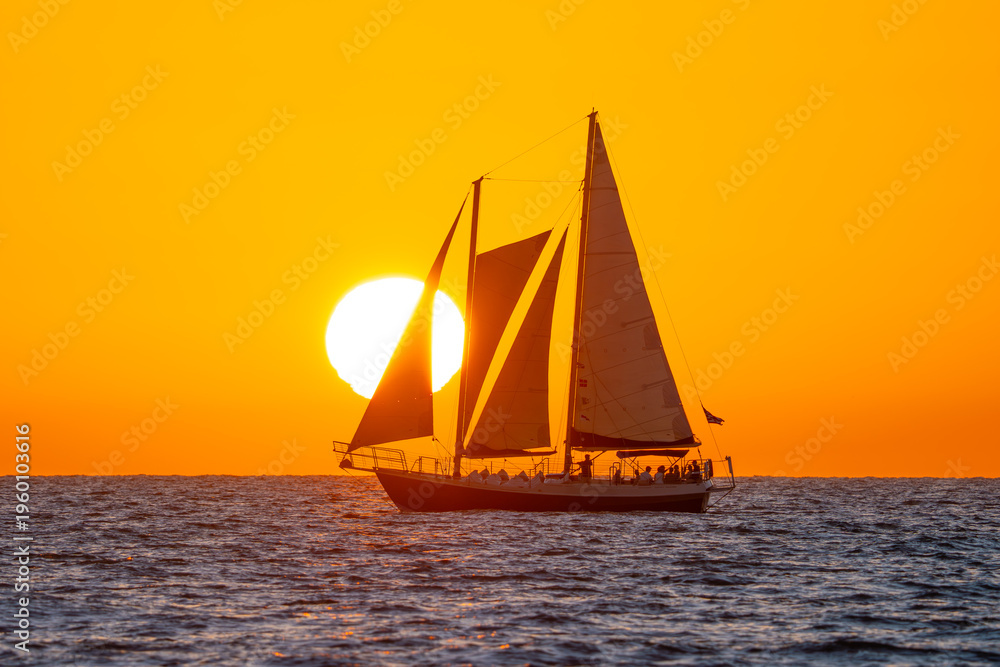 Fototapeta premium Sunset and Sailing yacht, Sailboat. Ocean sunset tour. Bright sun and warm orange sky. Calm sea, soft waves create a peaceful travel and vacation scene with relaxing coastal atmosphere. Gulf of Mexico