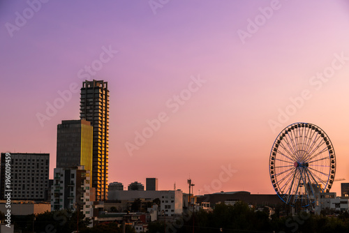Modern skyline featuring Estrella de Puebla Ferris wheel and illuminated skyscrapers against vibrant purple and pink sunset sky in Puebla, Mexico