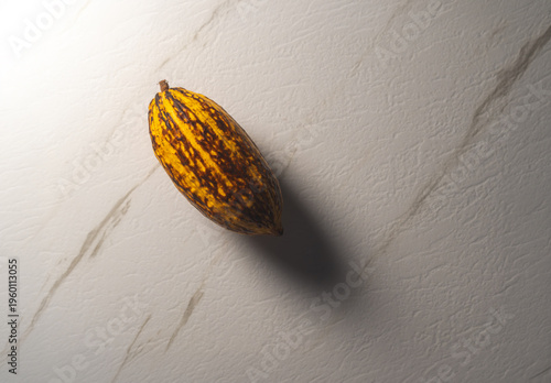 Mazorca de cacao entera sobre superficie de mármol blanco con iluminación dramática