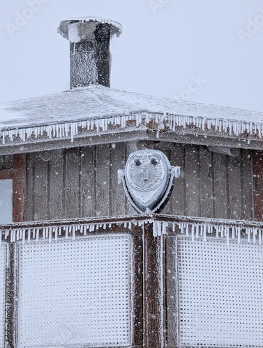 Canvas-taulu Frozen coin-operated telescope  binoculars covered in rime ice for viewing at a ski resort, on top of a mountain and shelter behind, ski season