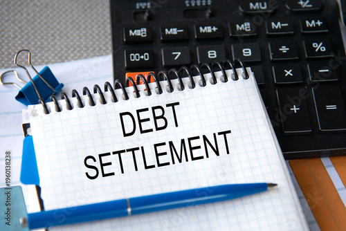 Notebook with the words DEBT SETTLEMENT in the notebook on the background of a black calculator