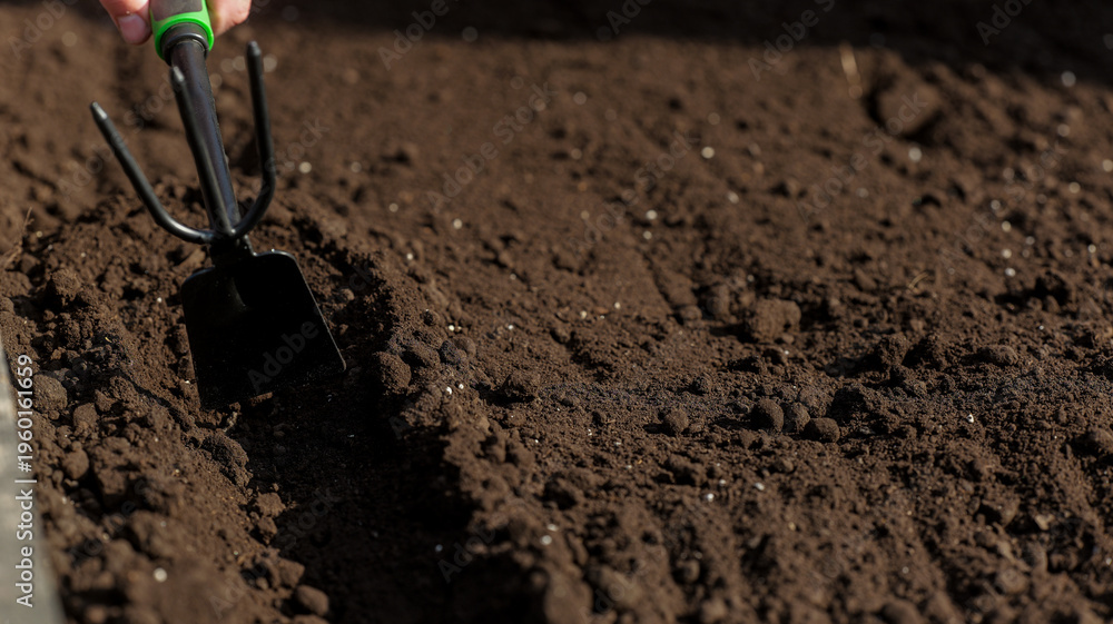 Αυτοκόλλητο Gardener preparing rich dark soil with a hand trowel for planting seeds or seedl