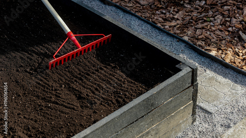 Tableau sur toile Gardener uses red rake to level dark soil in a raised garden bed