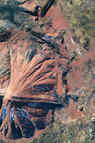Red industrial slagheap with eroded gullies and snow traces forming a dramatic alien-like surface texture in a high-angle detailed aerial shot.