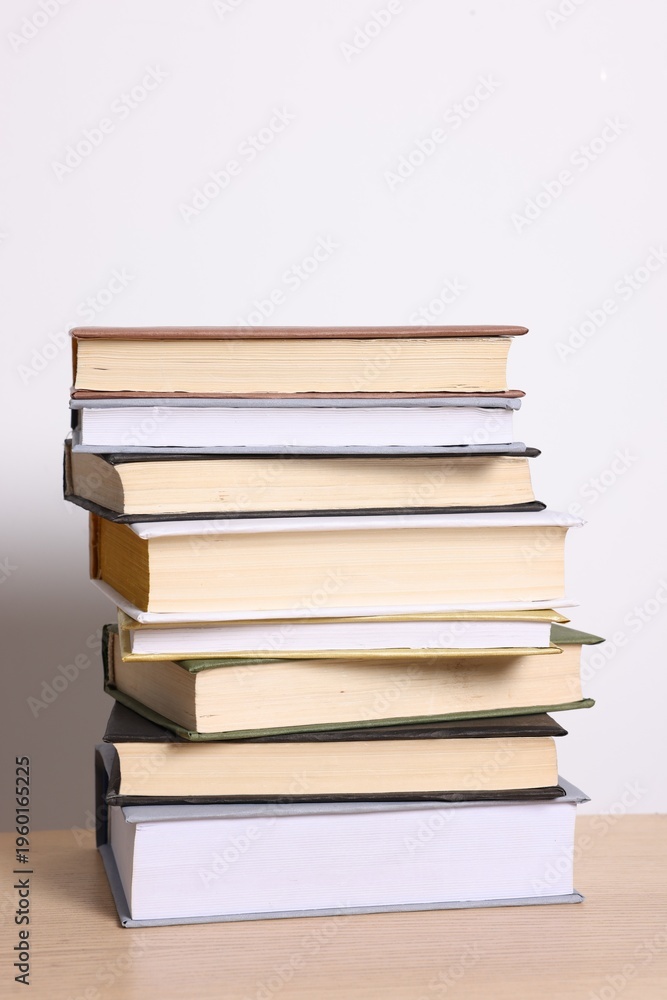 Fototapeta premium Stack of different books on wooden table against light background