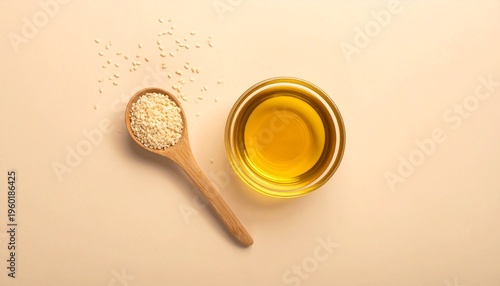 Overhead view of sesame seeds in a wooden spoon next to a glass bowl of sesame oil on a light beige background.