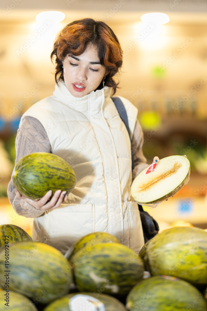 Fototapeta premium Young woman buyer choosing fresh melon at vegetable market