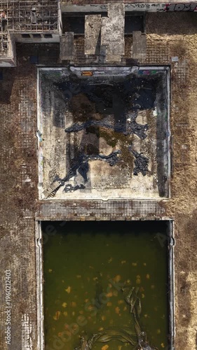 Top-down drone shot of derelict industrial area featuring empty concrete basins, stagnant water, debris, and weathered surfaces, illustrating decay, neglect, and urban abandonment.