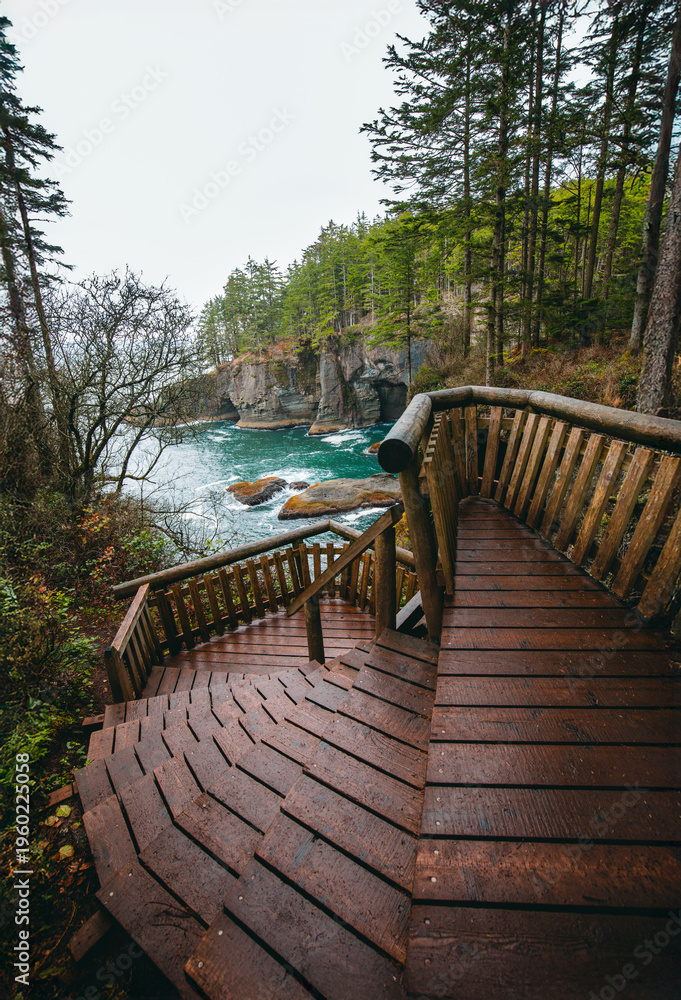 Obraz premium A wooden staircase descends along a rugged coastal cliff overlooking turquoise ocean water at Cape Flattery, Olympic National Park