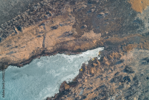 Frozen shoreline of a small lake with dry reeds and frost, winter ecosystem and environmental protection, aerial drone perspective