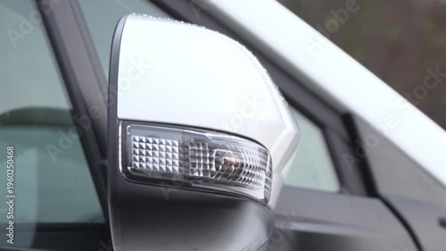 Orange turn signal indicator blinking on white car side mirror. safety signal activated on a white car exterior.