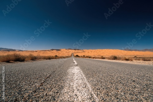 Straight Gravel Road Leading Through Arid Desert Landscape Under a Clear Deep Blue Sky with Distant Hills and Sparse Vegetation
