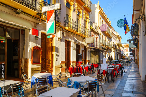 Billede på lærred A narrow alley of sidewalk cafes and restaurants in the historic old town center of the Andalusian city of Ronda, Spain