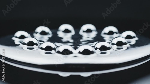 Liquid mercury droplets on a dark reflective surface forming a seamless loop